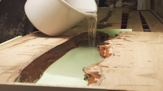 Carpenter pouring epoxy resin over wooden table. Furniture manufacture.