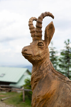 Wooden statue and sculpture of chamois. Blurred mountain cabin and hut in the background. Shallow focus.