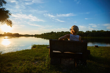 Fototapeta premium Woman Sitting On Bench During A Beautiful Sunset