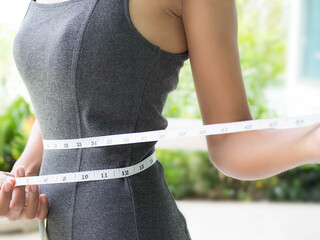 Close up waist with measuring tape on blur background for weight loss article or diet. Shapely girl...