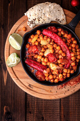 Spicy chickpeas with hot red peppers, tomatoes, cumin, garlic and other spices in a frying pan on a black background top view. Chickpeas stewed with vegetables and spices, oriental cuisine. 