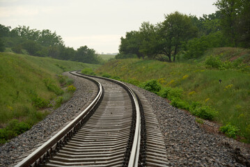Railroad meanders among green slopes summer day