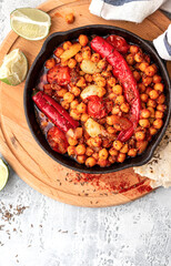 Spicy chickpeas with hot red peppers, tomatoes, cumin, garlic and other spices in a frying pan on a grey background top view. Chickpeas stewed with vegetables and spices. Free space for text