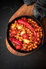 Spicy chickpeas with hot red peppers, tomatoes, cumin, garlic and other spices in a frying pan on a black background top view. Chickpeas stewed with vegetables and spices, oriental cuisine. 