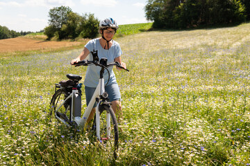 Fahrrad Fahrerin schiebt an einem schönen Sommertag ihr Fahrrad durch eine blühende Sommerwiese.