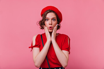 Fototapeta premium Dark-eyed french woman expressing amazement. Studio portrait of surprised glamorous girl in red beret.