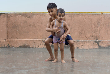 Fototapeta na wymiar Two Wet Kids Playing and having Fun in Rain at their Terrace, Outdoors during Monsoon Season.