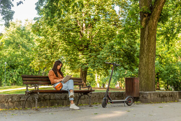 A young woman is sitting on a park bench with the book in her han
