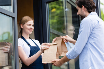 Attractive saleswoman giving paper bags to man near door of cafe
