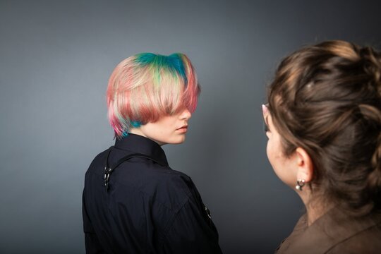 Female hairdresser designing the hair of a young girl in red, blue and green colors.