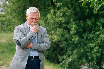 Fototapeta premium An elderly man stands wistfully smiling in an outdoor park.