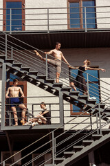 The group of modern ballet dancers performing on the stairs at the city. Fast moving of citylife, grace in daily things around. Graceful and flexible models in sunshine with buildings on background.