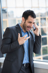 manager moro vestito con giacca nera e camicia blu, in piedi di fronte a una vetrata si arrabbia...