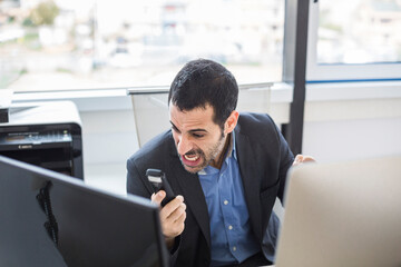 manager moro vestito con giacca nera e camicia blu, seduto nella sua postazione di lavoro si...