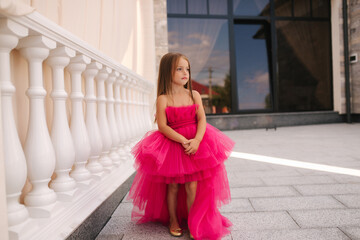 Adorable little girl model in pink fluffy dress walkin outdoors by the restaurant. Happy little kid