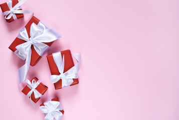 Many red boxes with a white ribbon on a pink background. Boxes with presents. View from above. Flatly