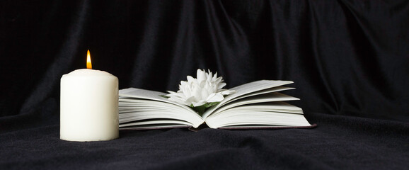 Condolence card. A white memorial candle with white flowers and an open book. The funeral, the sadness.