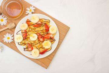 Trendy food - pancake cereal. Heap of mini cereal pancakes on a white plate, copy space. Strawberries, bananas, and honey. A beautiful and healthy Breakfast. Top view.