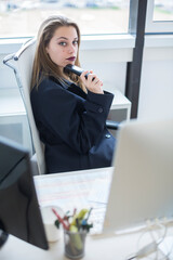 manager bionda vestita in giacca scura è seduta nella sua postazione di lavoro mentre utilizza il telefono 