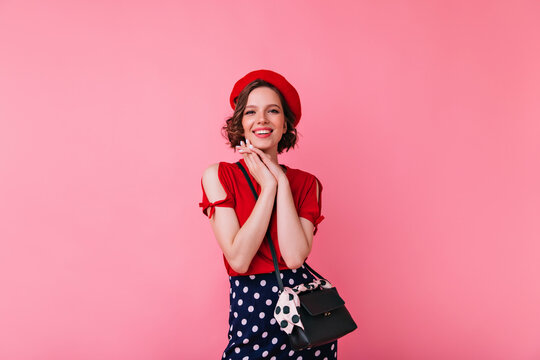 Magnificent white girl in glamorous outfit posing on pink background. Jocund french woman in beret standing with cute smile.