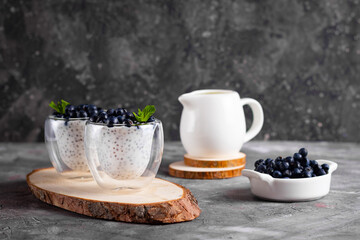 Chia pudding with mint in glasses on a wooden stand with a plate of blueberries with creamer
