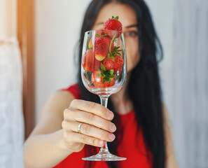 Young girl holding glass goblet with red strawberries at face level