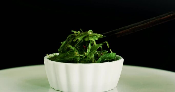 Japanese food concept. Fresh seaweed salad with sesame seeds in white bowl on black background.