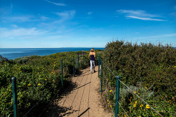 Wide angle view of short haired blonde women in her 40s in jeans and black top walking on dirt...