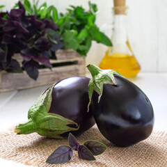 Fresh eggplants and aromatic herbs on a white wooden background.