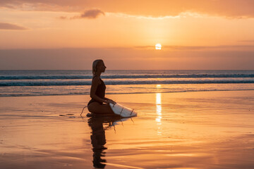 Fototapeta premium Portrait of surfer girl with beautiful body on the beach with surfboard at colourful sunset time.