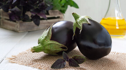 Fresh eggplants and aromatic herbs on a white wooden background.