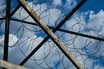 Rusty Metal Construction with Barbed Wire against a Blue Sky with light light clouds. Background image symbolizing the restriction of freedom and the opposition of brute strength and fragile nature
