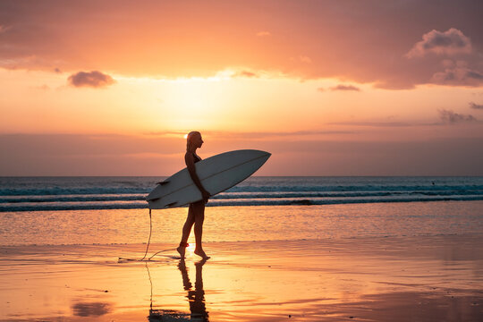 Portrait of surfer girl with beautiful body on the beach with surfboard at colourful sunset time