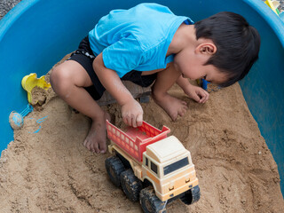 Asian child boy playing car toy in sandbox outdoor with smiling face. Happy kid enjoy in relaxing day.