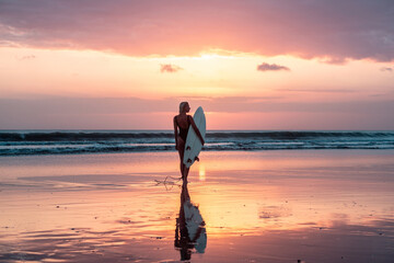 Portrait of surfer girl with beautiful body on the beach with surfboard at colourful sunset time..