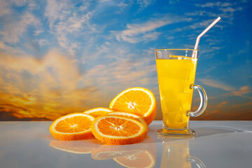 Fresh orange juice with ice in glass on sunrise background