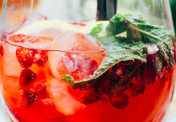 summer cocktail with mint leaf, lemon slices and red berries with pomegranate and ice cubes,