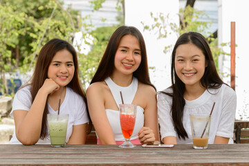 Three happy young Asian women as friends having drinks together at the coffee shop outdoors