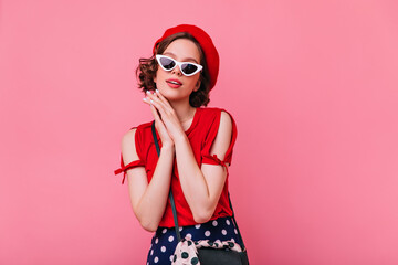 Graceful pale girl in french beret standing on pastel background. Optimistic brunette woman in sunglasses posing in studio.