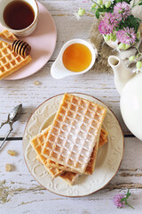 Belgian waffles and honey, cup of tea for sweet spring breakfast with clover flowers