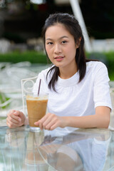 Young beautiful Asian woman sitting at the coffee shop outdoors