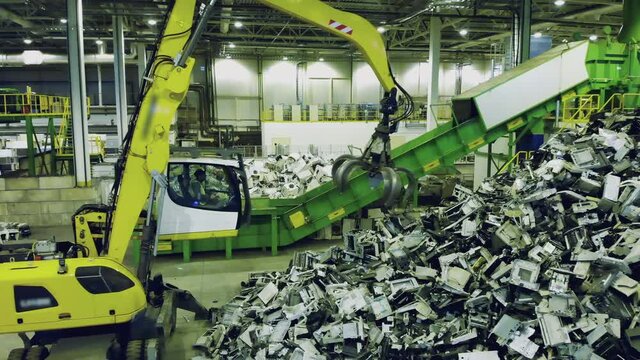 Trash, e-waste, electronic garbage recycling factory. Excavator grabs garbage and puts it onto factory conveyor.