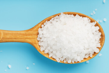 Sea salt in a wooden spoon on a blue background, with scattered salt.