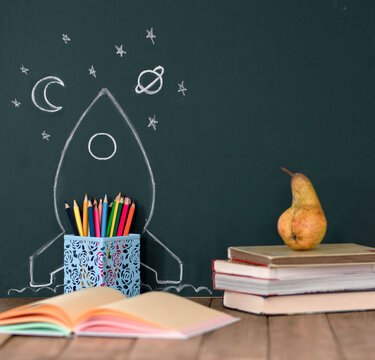 Back to School Concept with Hand Drawn Rocket and stars on Blackboard. Colored pencils and books on a wooden table. Copy space for text.