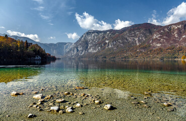 Fototapeta na wymiar Beautiful sunny landscape. View on mountain lake with crystal clear azure water in Julian Alps. Slovenia. Awesome Autumn landscape. Bohinj Lake. Triglav National Park
