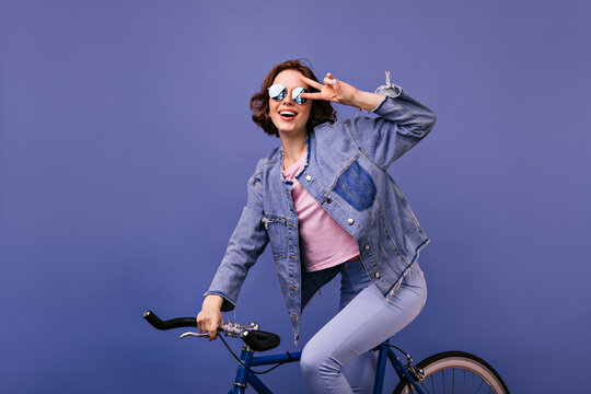 Beautiful short-haired girl in sparkle glasses sitting on bike. Cheerful female model posing on bicycle and expressing happiness. - Powered by Adobe