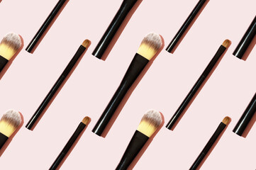 A pattern of black makeup brushes. Modern bright decorative background. Women's accessories on a pink background. Professional makeup artist's tool for applying eyeshadow and foundation