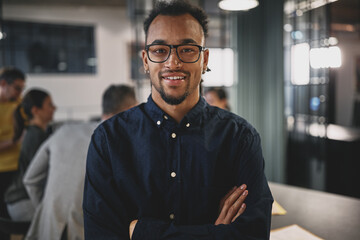 Smiling young businessman standing with his arms crossed at work