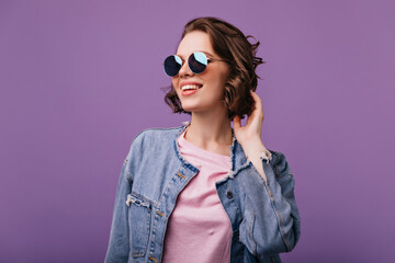 Naklejka premium Appealing young woman in sparkle sunglasses looking in distance. Portrait of glamorous european model with short haircut smiling on purple background.