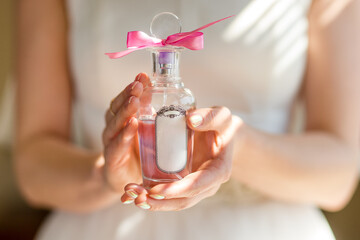 Bottle perfume in bride hands. Female hands holding a bottle of elite perfume. Mock-up with blank transparent bottle.